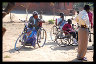 Crippled adults wait in the sun on makeshift, hand powered bicycles
