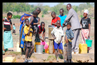 Pastor Stanley Mateya using hand pump at a borehole, surrounded by orphan children